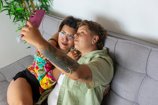 Casual lesbian couple selfie time on cozy modern sofa at home