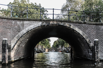 Fototapeta premium Amsterdam, Netherlands architectural photography, Amsterdam Canal with Historic Dutch Houses at Sunset, Cyclist Riding Through Amsterdam’s Charming Streets, Houseboats and Bridges Along the Amsterdam