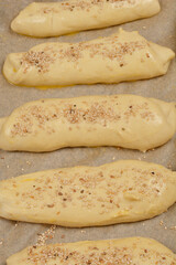 A top-down shot of uncooked dough rolls sprinkled with sesame seeds on a baking sheet, ready for baking