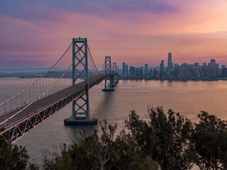 The Bay Bridge spans the water to connect to the San Francisco skyline at sunset in California,...