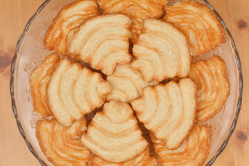 A top-down view of a glass plate filled with golden-brown palmiers, showcasing their flaky texture and spiral shape