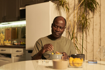 African American senior man in casual attire sitting by kitchen table on sunny morning and mixing...