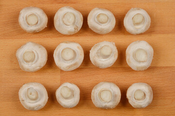 A top-down view of twelve white button mushrooms arranged in a rectangular grid on a light wooden surface
