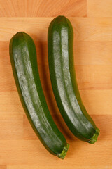 Two whole zucchinis are placed diagonally on a light wooden cutting board, showcasing their dark green skin