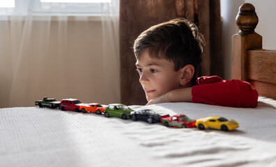 boy in a red shirt lines up toy cars on his bed. signs of autism spectrum disorder (ASD) autism or...