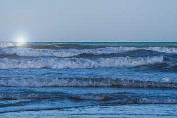 A light storm on the Spanish coast. Sea waves with crests of white foam roll onto a sandy beach on...