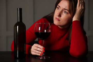 Alcohol addiction. Woman with glass of red wine and bottle at wooden table indoors