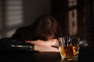 Alcohol addiction. Woman at table indoors, focus on glass of whiskey