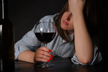 Alcohol addiction. Miserable woman with wine at table in dark