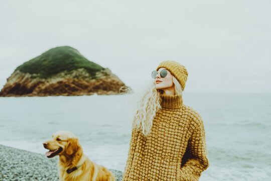 Caucasian woman in yellow sweater by ocean with dog on foggy day