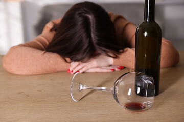 Alcohol addiction. Miserable woman with wine at table indoors, selective focus