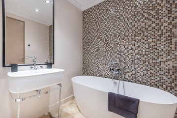 Stylish bathroom interior design. The bathtub is against a wall decorated with dark mosaic tiles.