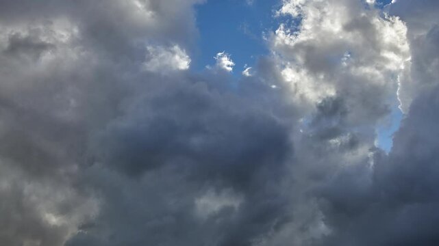 Timelapse of a flock of stormy clouds that cover a blue sky with the sun behind.