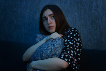 Fear of darkness. Scared young woman hugging pillow on couch indoors at night