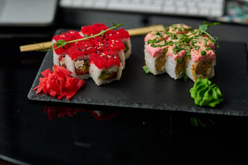 Sushi roll on black plate with chopsticks and laptop on black background