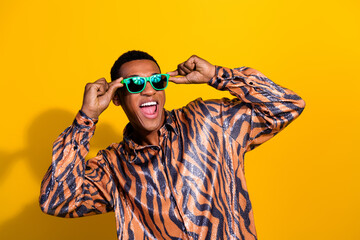 Vibrant young man enjoying in a tiger-print shirt and green glasses against a bright yellow...
