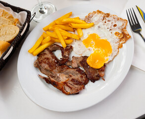 Cooked tender veal with fried egg and French fries. Serving a Spanish meat dish on a white plate