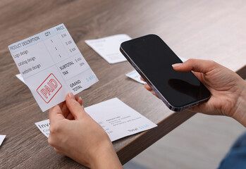 Paying bills. Woman with different invoices and phone at wooden table indoors, closeup