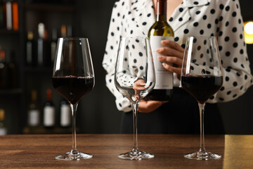 Professional sommelier with glasses and bottle of red wine at wooden table indoors, closeup