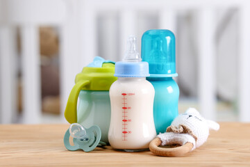 Feeding bottles with milk, toy and pacifier on wooden table indoors