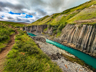 A scenic view of Studlagil Canyon in Iceland with basalt columns and a turquoise river.