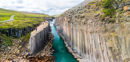 A scenic view of Studlagil Canyon in Iceland with basalt columns and a turquoise river.