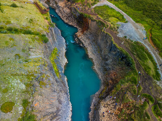 A scenic view of Studlagil Canyon in Iceland with basalt columns and a turquoise river.