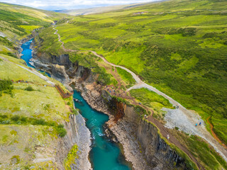 A scenic view of Studlagil Canyon in Iceland with basalt columns and a turquoise river.