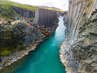 A scenic view of Studlagil Canyon in Iceland with basalt columns and a turquoise river.