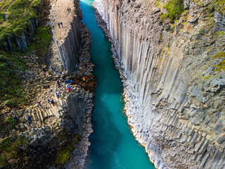 A scenic view of Studlagil Canyon in Iceland with basalt columns and a turquoise river.
