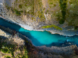A scenic view of Studlagil Canyon in Iceland with basalt columns and a turquoise river.
