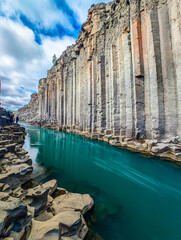 A scenic view of Studlagil Canyon in Iceland with basalt columns and a turquoise river.