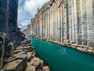 A scenic view of Studlagil Canyon in Iceland with basalt columns and a turquoise river.
