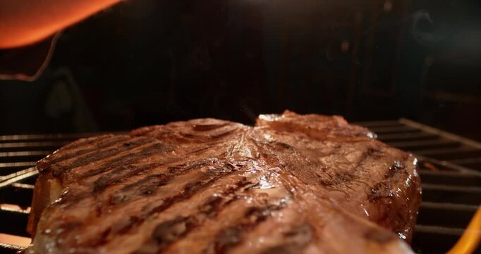 Dolly out shot of a piece of T Bone steak being flame grilled to perfection
