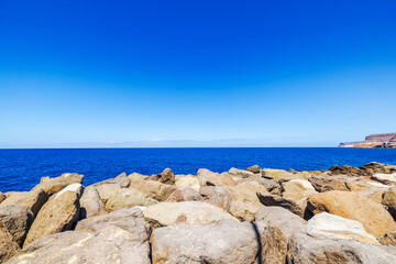 Rocky coastline of Atlantic Ocean on Gran Canaria under clear blue sky.