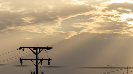 Silhouette of electric pole and sky with sunlight at sunset.