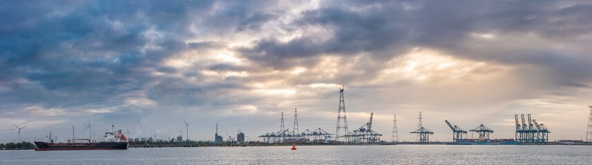 Fototapeta premium Cargo ship navigates through the bustling port of Antwerpen under a cloudy sky