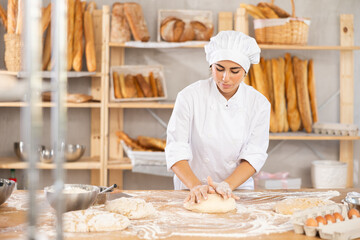 Young woman baker kneading dough for baking on table