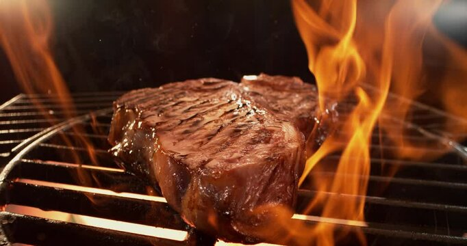 Slow-motion shot of a juicy  T Bone steak sizzling on the grill with fire flame in the background. Close-up footage