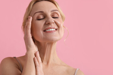 Smiling middle aged woman on pink background. Space for text