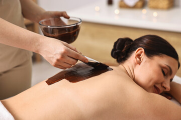 Chocolate body wrap. Spa worker applying mask onto woman's back in salon, closeup