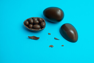 A broken chocolate Easter egg spills chocolate-covered treats on a vibrant blue background. Perfect for festive, dessert, and confectionery-themed visuals.
