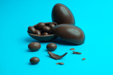 Chocolate Easter eggs with a glossy finish, one broken open to reveal chocolate-coated treats, placed on a vibrant blue background. A perfect festive and confectionery-themed composition.