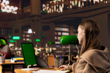 College student looks at a copy space screen on tablet while collecting notes from reliable academic sources, consulting the campus library books collection for an assignment. Student life.