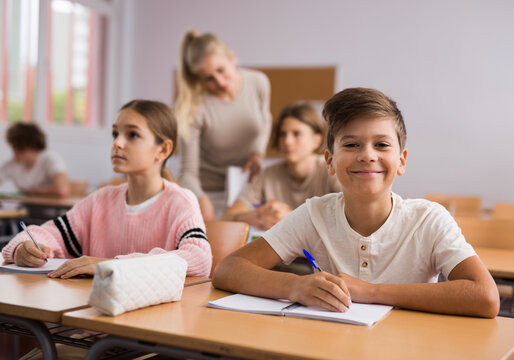 Young girl and smiley boy sitting at desk in classroom during lesson in school.
