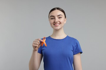 Multiple Sclerosis awareness. Happy young woman holding orange ribbon on light grey background