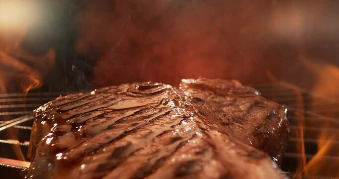 Dolly out shot macro shot of grilling a T Bone steak on the flaming grill in black background 