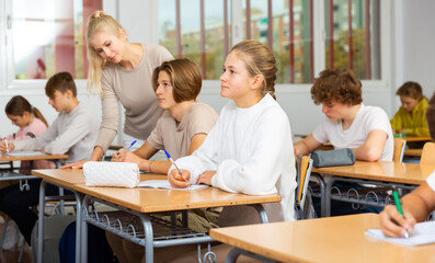 Group of teenage girls and boys exercising during lesson in classroom.