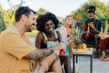 Friends enjoying colorful cocktails, laughing and talking by the pool during a summer party