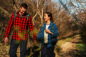 Interracial couple hiking hand in hand along a scenic trail in the woods, soaking up the warmth of a sunny day while embracing the beauty of nature and each others company
